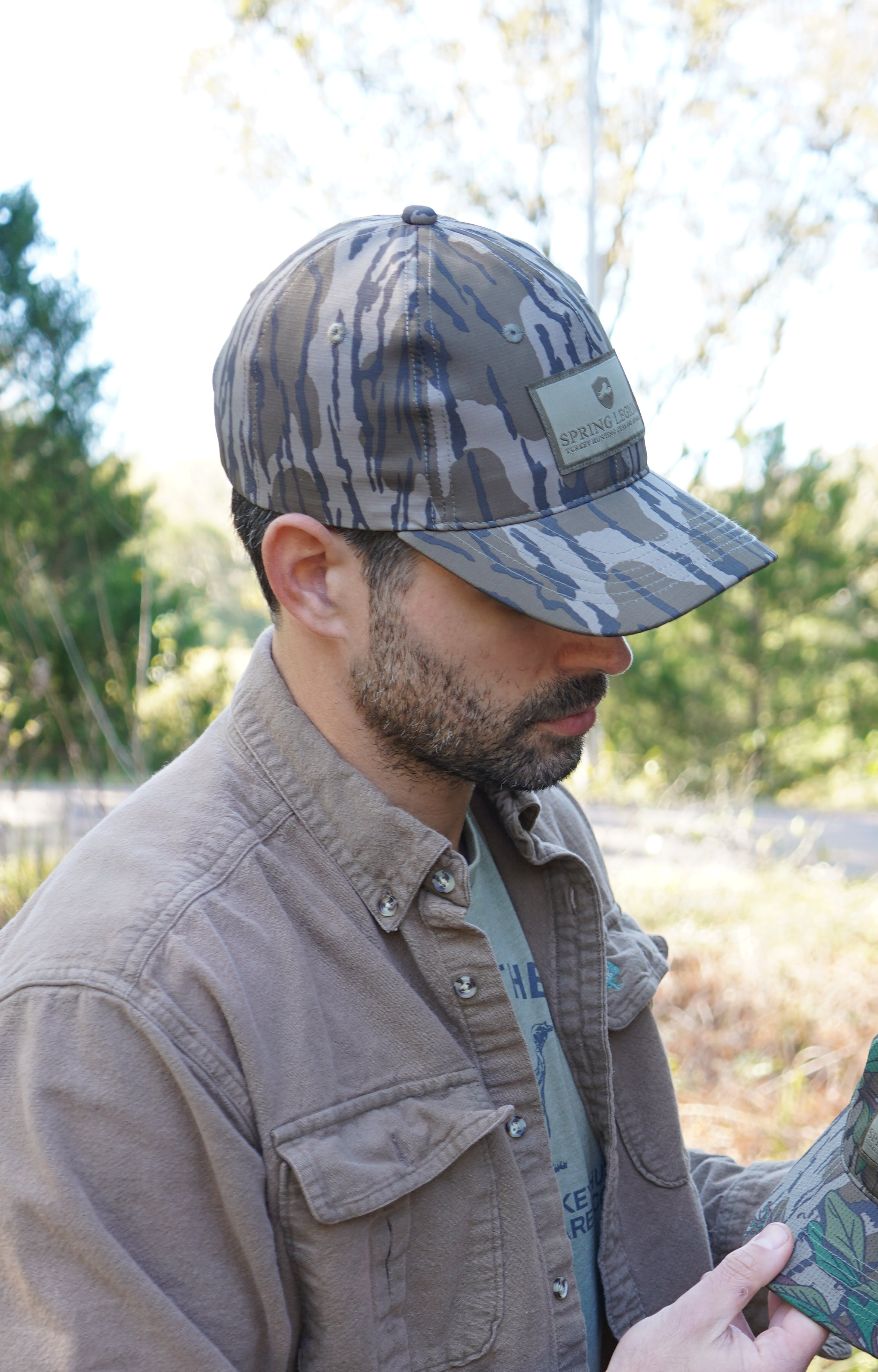 Man wearing a camouflage hunting cap and jacket outdoors with trees in the background