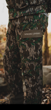 Camouflage pants with 'Spring Legend' logo in a natural setting
